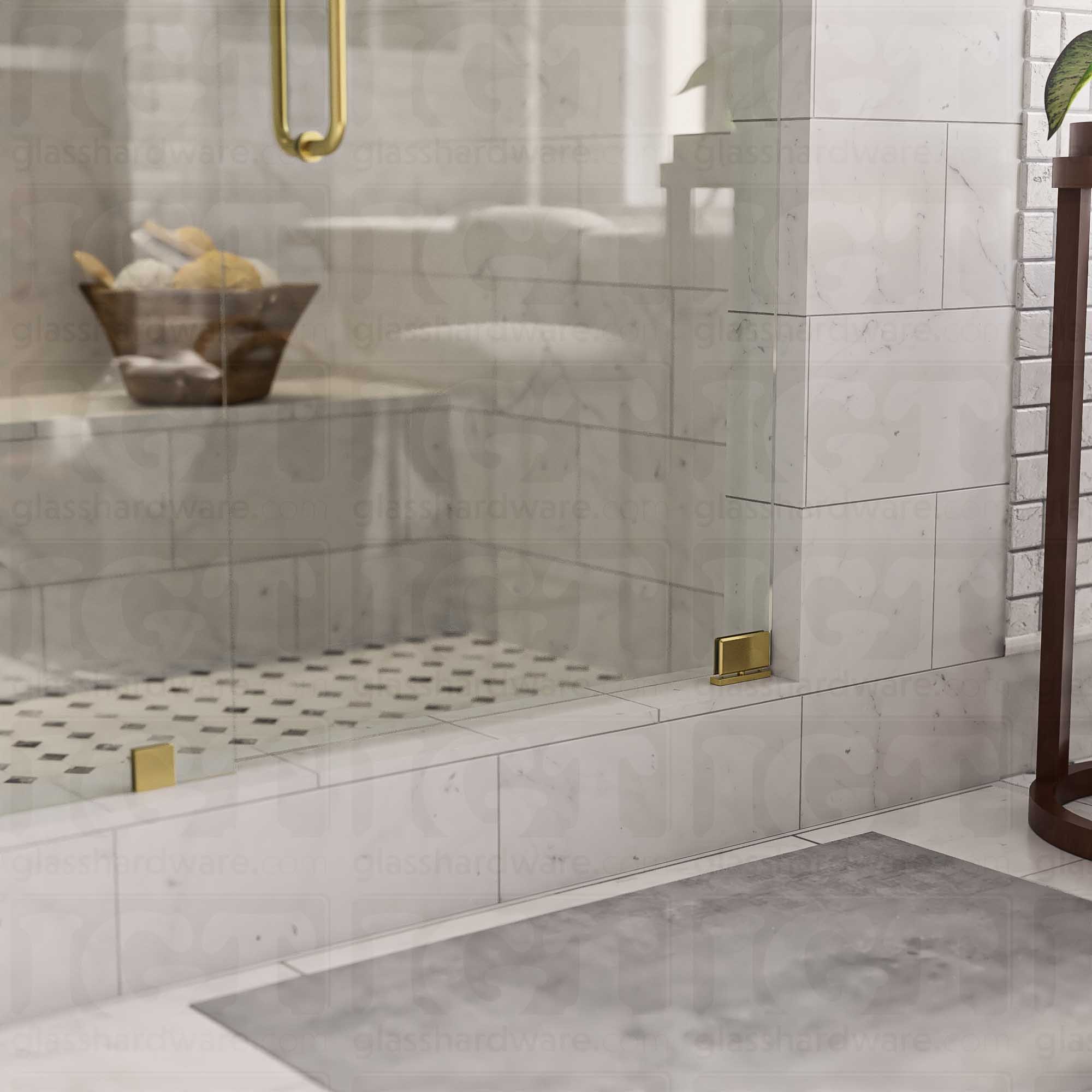 The Top and Bottom Bilboa Pivot Hinge mounted at the bottom of the glass shower door, attached securely to the tiled threshold. The hinge's Gold Brushed finish coordinates with the matching glass clamps and round pull handle, creating a cohesive and elegant look.