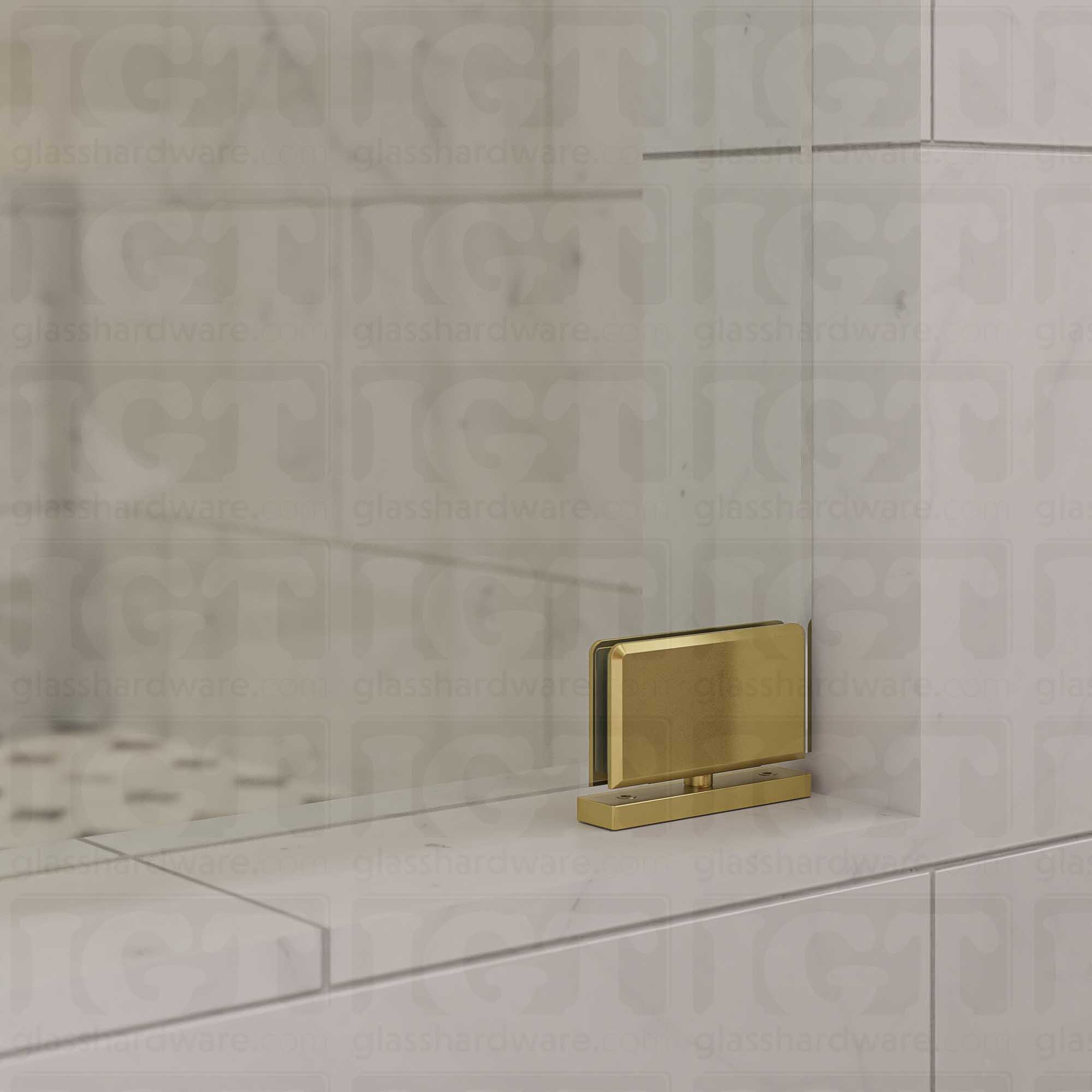 Close-up of a Top and Bottom Bilboa Pivot Hinge mounted at the bottom of the glass shower door, attaching it securely to the tiled threshold. Gold Brushed.