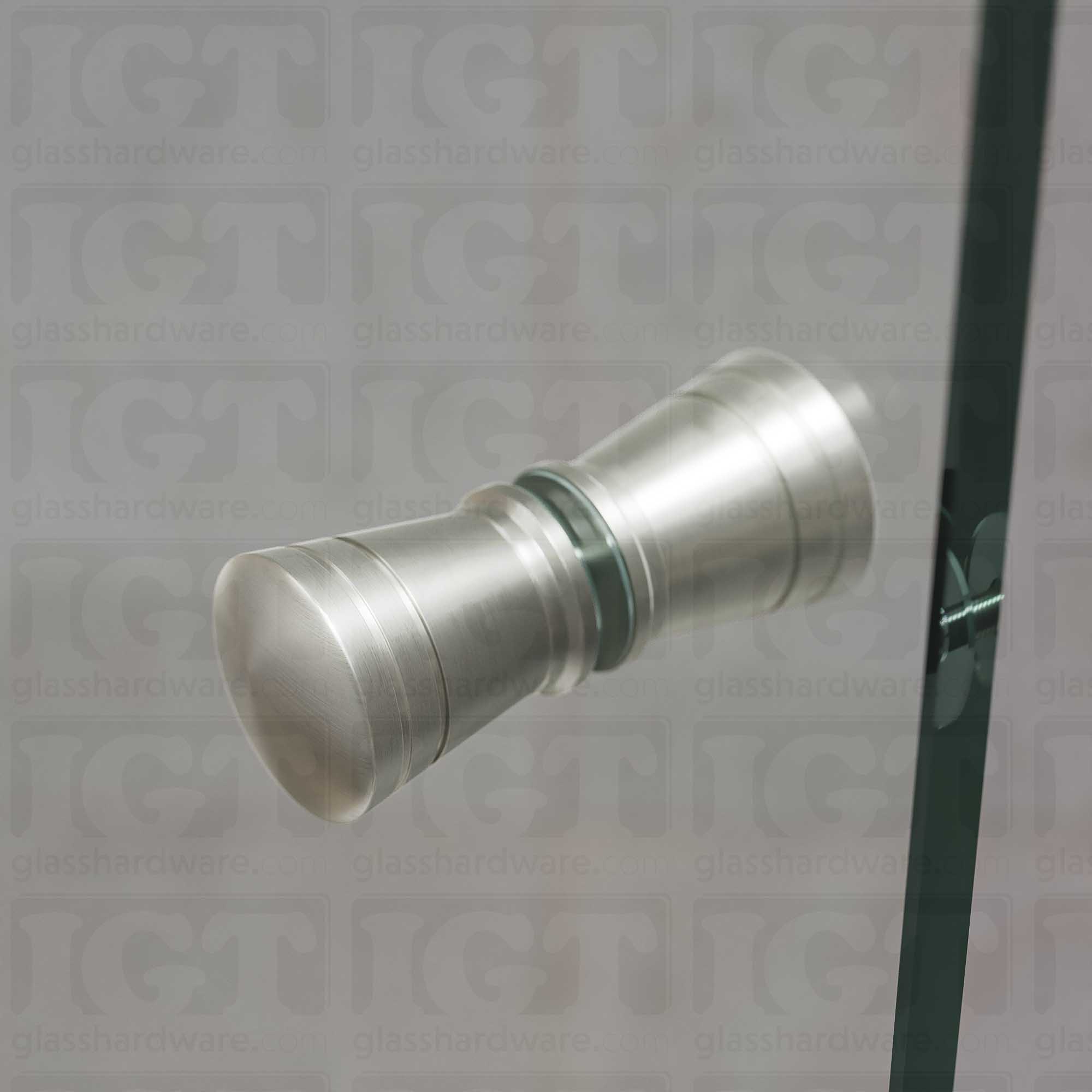 A close up of the Modern Ribbed Bow Tie Back-to-Back Door Knob installed on a glass shower door. Soft ambient light highlights the knob's Brushed Nickel finish.