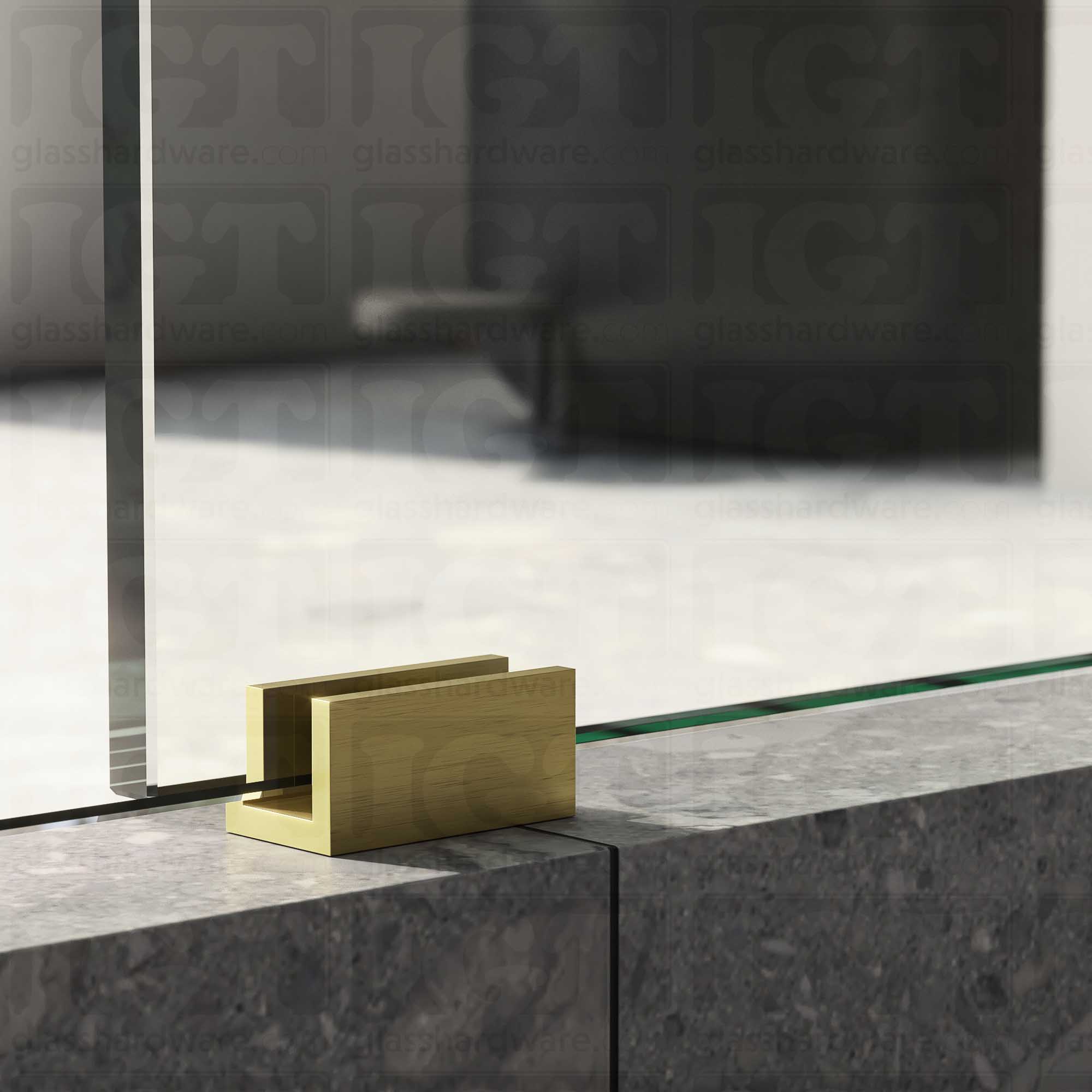 A close up of the Floor Guide for Modern Sliding System installed at the base of a glass sliding door, showcasing it's Gold Brushed finish.