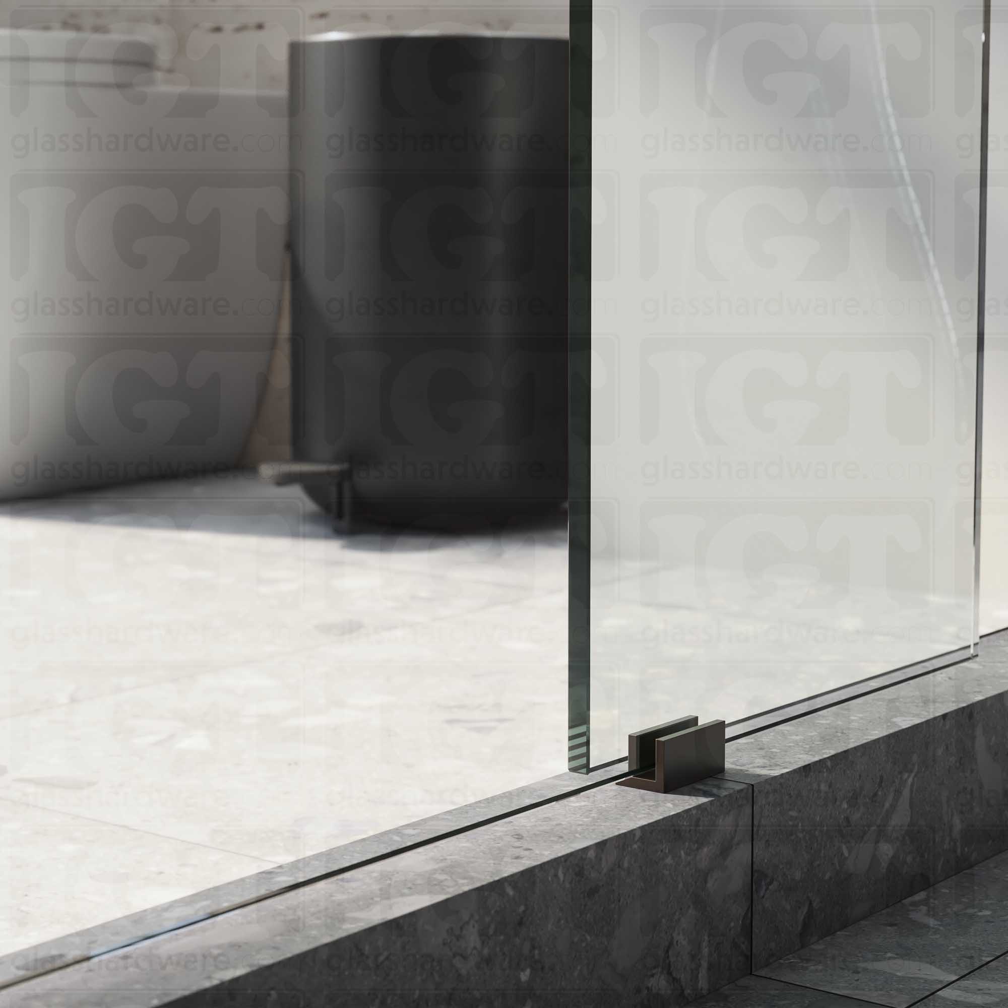 A close up of the Floor Guide for Modern Sliding System installed at the base of a glass sliding door. Oil Rubbed Bronze.