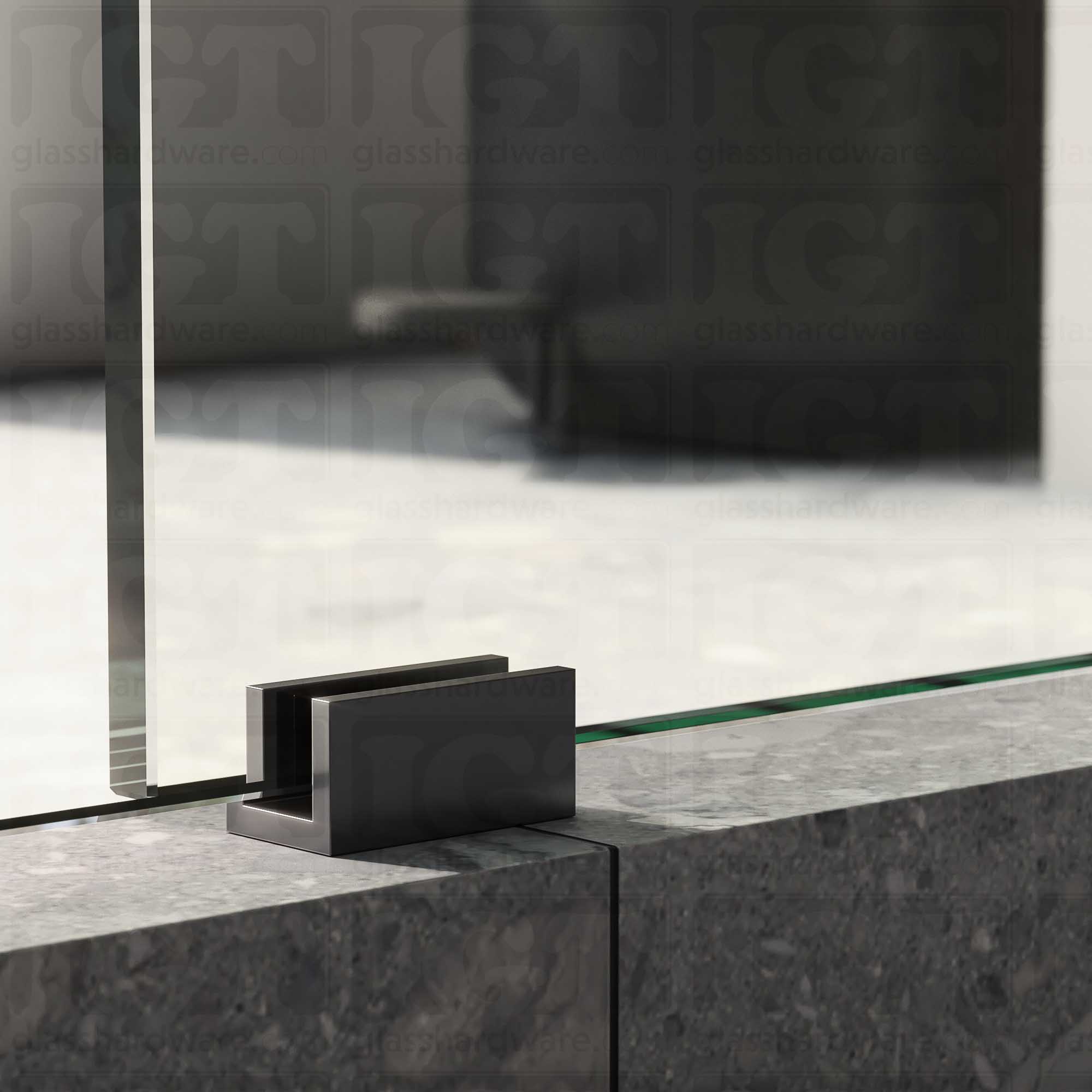 A close up of the Floor Guide for Modern Sliding System installed at the base of a glass sliding door, showcasing it's Polished Gun Metal finish.