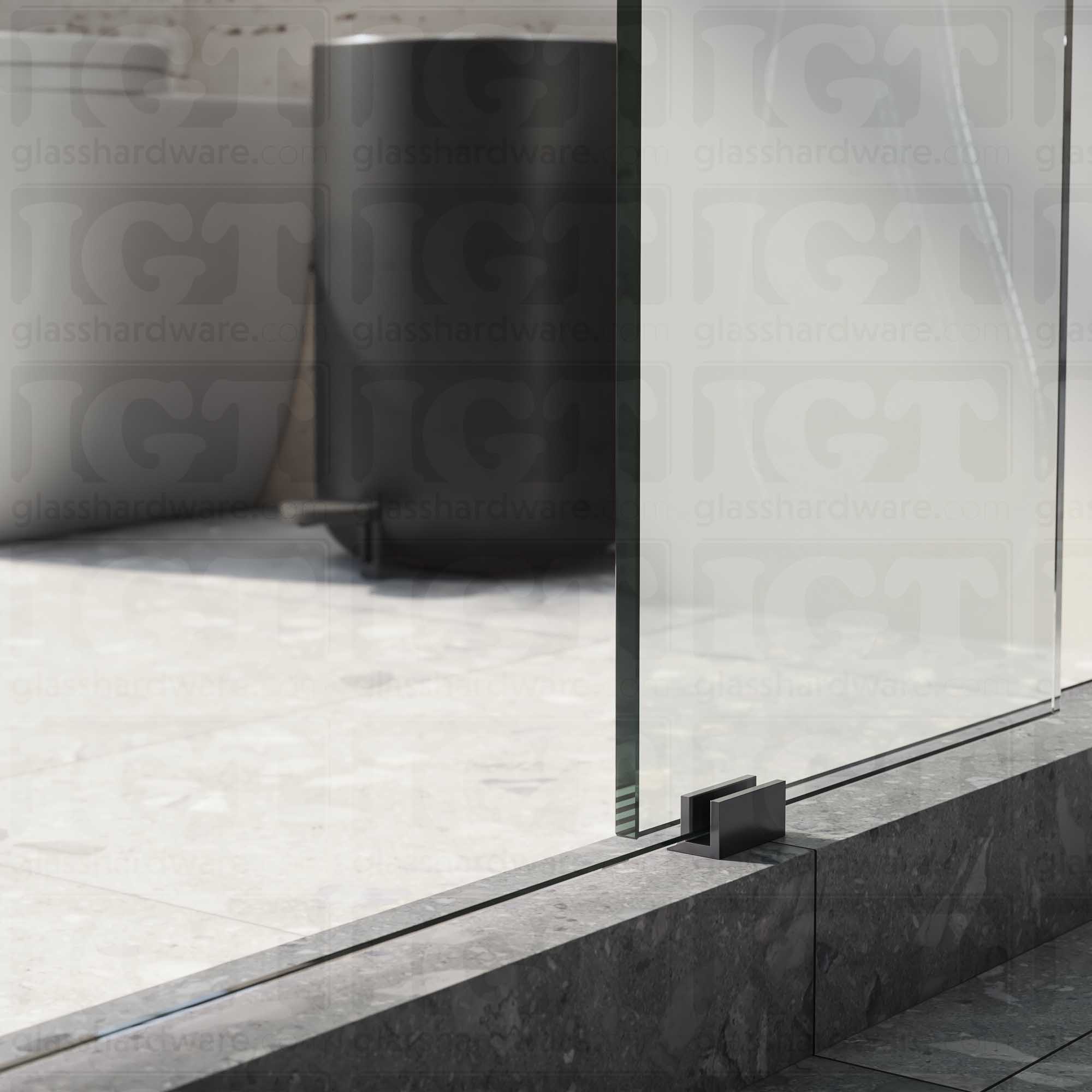 A close up of the Floor Guide for Modern Sliding System installed at the base of a glass sliding door. Polished Gun Metal.